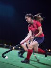 Determined young female field hockey player playing on field at night — Stock Photo