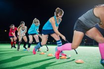 Jóvenes jugadoras de hockey sobre hierba practicando ejercicios deportivos en el campo por la noche - foto de stock