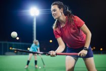 Giovane giocatore di hockey su prato femminile che rimbalza palla sul bastone da hockey, esercitandosi sul campo di notte — Foto stock
