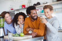 Multi-étnica família fazendo e bebendo smoothie verde saudável na cozinha — Fotografia de Stock