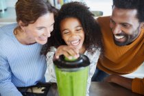 Laughing multi-ethnic family making healthy green smoothies in blender in kitchen — Stock Photo
