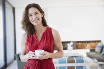 Портрет улыбается, уверенная брюнетка женщина пьет кофе в гостиной — стоковое фото
