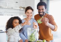 Lächelnde multiethnische Familie macht grünen Smoothie im Mixer in der Küche — Stockfoto