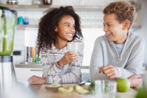 Sorrindo irmão e irmã bebendo smoothie verde saudável na cozinha — Fotografia de Stock