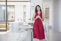 Retrato sorrindo morena no vestido vermelho bebendo café na sala de jantar — Fotografia de Stock