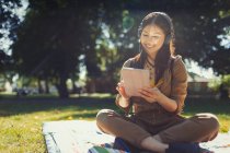 Улыбающаяся молодая женщина с цифровым планшетом, слушающая музыку с наушниками в солнечном летнем парке — стоковое фото