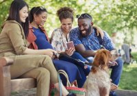Smiling friends with dog using smart phone in park — Stock Photo