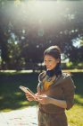 Улыбающаяся молодая женщина в наушниках с цифровым планшетом в солнечном летнем парке — стоковое фото