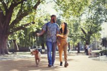 Feliz jovem casal andando cão no parque ensolarado — Fotografia de Stock