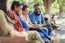Smiling friends using digital tablet on park bench — Stock Photo