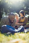 Lächelnder junger Mann, der mit dem Handy SMS schreibt und sich im sonnigen Sommerpark entspannt — Stockfoto