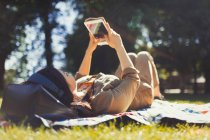 Молода жінка використовує цифровий планшет у сонячному літньому парку — стокове фото
