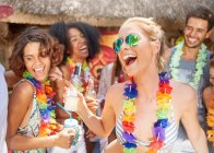 Playful friends wearing leis drinking and partying at sunny summer poolside — Stock Photo