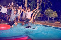 Portrait exuberant young friends jumping into swimming pool at night — Stock Photo
