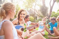 Jóvenes amigas pasando el rato, tocando la guitarra y bebiendo cerveza en la hierba de verano - foto de stock
