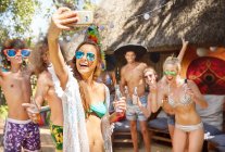 Энергичные молодые друзья пьют и делают селфи на солнечной летней вечеринке у бассейна — стоковое фото