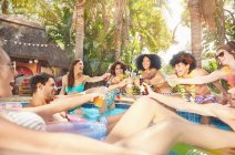 Захоплені друзі п'ють, тости пивні пляшки і коктейлі на літній вечірці басейну — стокове фото