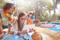 Young women friends hanging out, using digital tablet at sunny summer poolside — Stock Photo