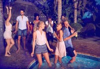 Молодые друзья танцуют и тусуются на летней вечеринке у бассейна по ночам — стоковое фото