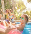 Ritratto giovane donna sorridente e sicura di sé che galleggia su una zattera gonfiabile nella soleggiata piscina estiva — Foto stock
