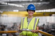 Портрет улыбающейся, уверенной в себе женщины-работницы с буфером обмена на платформе на заводе — стоковое фото