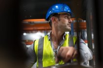 Trabalhador masculino que conduz empilhadeira, olhando sobre o ombro na fábrica — Fotografia de Stock