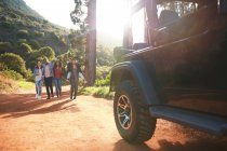 Junge Freunde laufen auf sonnigem Feldweg im Wald auf Jeep zu — Stockfoto