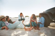 Jovem com câmera digital fotografar amigos pendurados na praia ensolarada — Fotografia de Stock