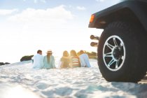Young friends relaxing, hanging out on beach behind jeep — Stock Photo