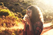 Junge Frau trinkt Kaffee im sonnigen Wald — Stockfoto