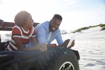 Sorridente giovane coppia utilizzando tablet digitale in jeep sulla spiaggia soleggiata — Foto stock