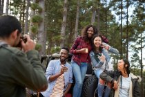 Young man with digital camera photographing friends at jeep in woods — Stock Photo