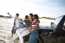Giovani amici con fotocamera telefoni prendere selfie a jeep sulla spiaggia soleggiata — Foto stock