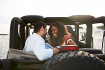 Affectueux jeune couple souriant sur le siège arrière de la jeep, profiter du voyage sur la route — Photo de stock