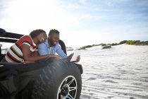 Junges Paar nutzt digitales Tablet im Jeep am sonnigen Strand und genießt Roadtrip — Stockfoto