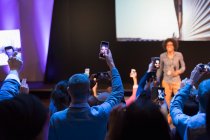 Зрители со смартфонами снимают спикера на сцене на конференции — стоковое фото