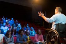 Спикер в инвалидной коляске на сцене разговаривает с аудиторией конференции — стоковое фото