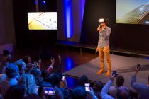 Audience watching male speaker with virtual reality simulator glasses on stage — Stock Photo