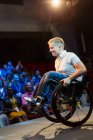 Smiling female speaker doing a wheelie in wheelchair on stage — Stock Photo