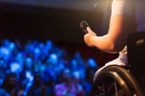 Женщина-спикер в инвалидной коляске держит микрофон на сцене — стоковое фото