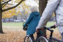 Senior mulher andar de bicicleta entre folhas de outono no parque — Fotografia de Stock