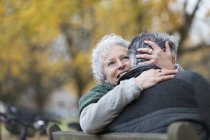 Sorrindo, casal idoso afetuoso abraçando no banco no parque de outono — Fotografia de Stock