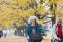 Sorridente, spensierata donna anziana in bicicletta tra gli alberi nel parco autunnale — Foto stock