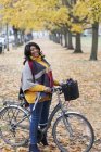 Retrato sonriente, mujer segura de montar en bicicleta entre árboles y hojas en el parque de otoño - foto de stock