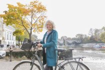 Retrato sonriente mujer mayor bicicleta a lo largo del río otoño - foto de stock