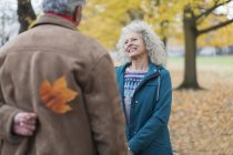 Marito più anziano giocoso che sorprende moglie con foglia di autunno in parco — Foto stock