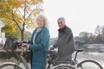 Retrato sonriente pareja de ancianos montar en bicicleta a lo largo del río otoño - foto de stock