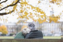 Cariñosa pareja de ancianos abrazándose en el banco en el parque de otoño - foto de stock