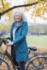 Улыбающийся портрет, уверенная старшая женщина катается на велосипеде в осеннем парке — стоковое фото