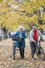 Couple aîné à vélo de marche entre les arbres et les feuilles dans le parc d'automne — Photo de stock